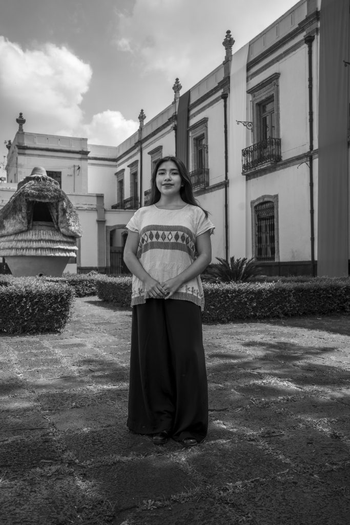 Retrato de Fátima Abril Zúñigam en blanco y negro. Viste ropa tradicional y detrás de ella se ve un edificio antiguo.